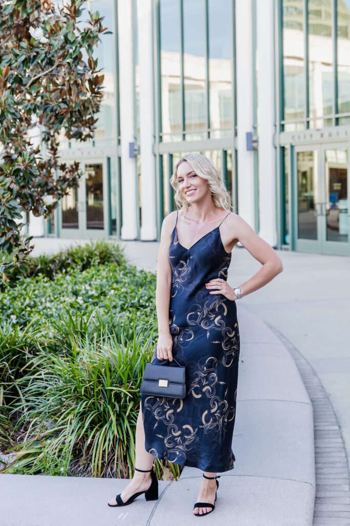 Personal stylist Jaquelyn Wahidi wears a black and gold slip dress in front of a civic building.