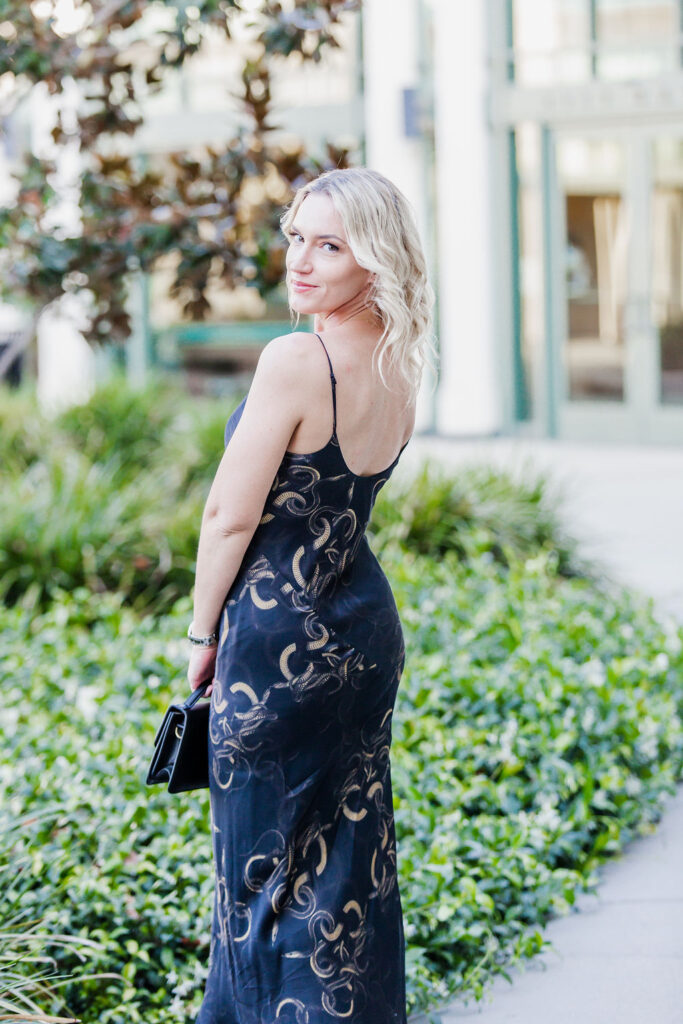 Personal stylist Jaquelyn Wahidi wears a black and gold slip dress in front of a civic building.