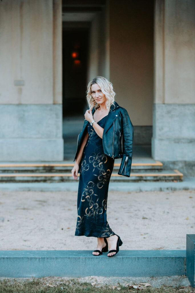 Personal stylist Jaquelyn Wahidi wears a black and gold slip dress in front of an art center.